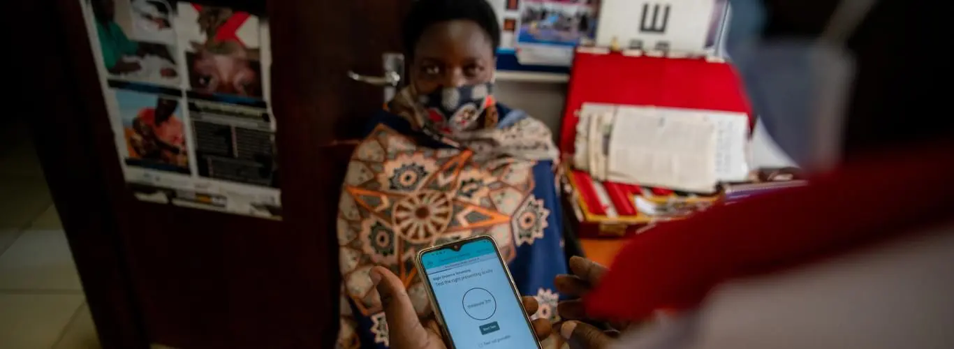 A woman in Uganda sits facing the camera while the screener looks at the Peek Capture app to prepare for vision screening.