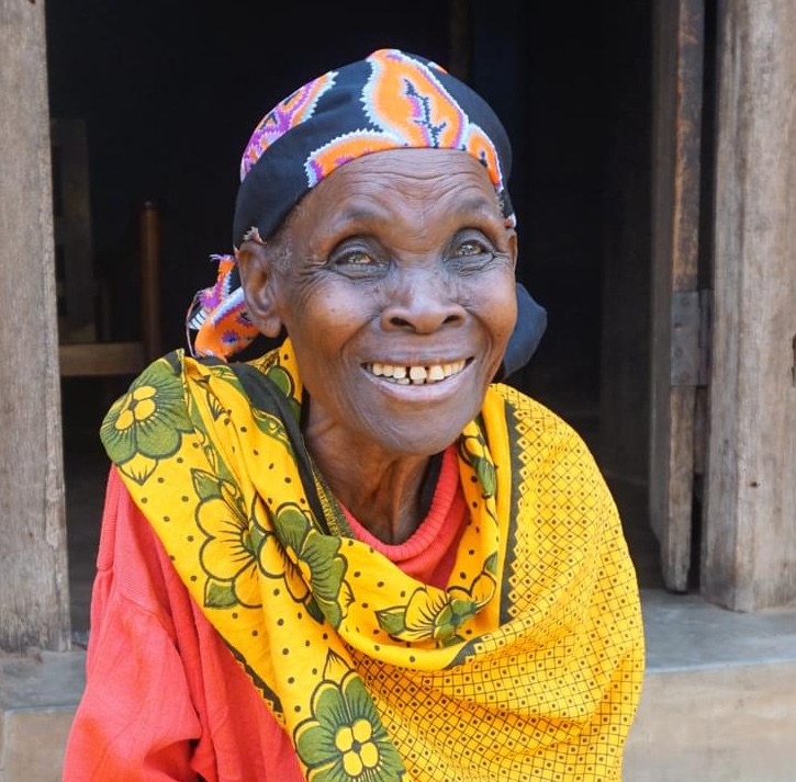 Teodosia, an elderly woman from Tanzania, smiles outside her home after having her cataracts removed.