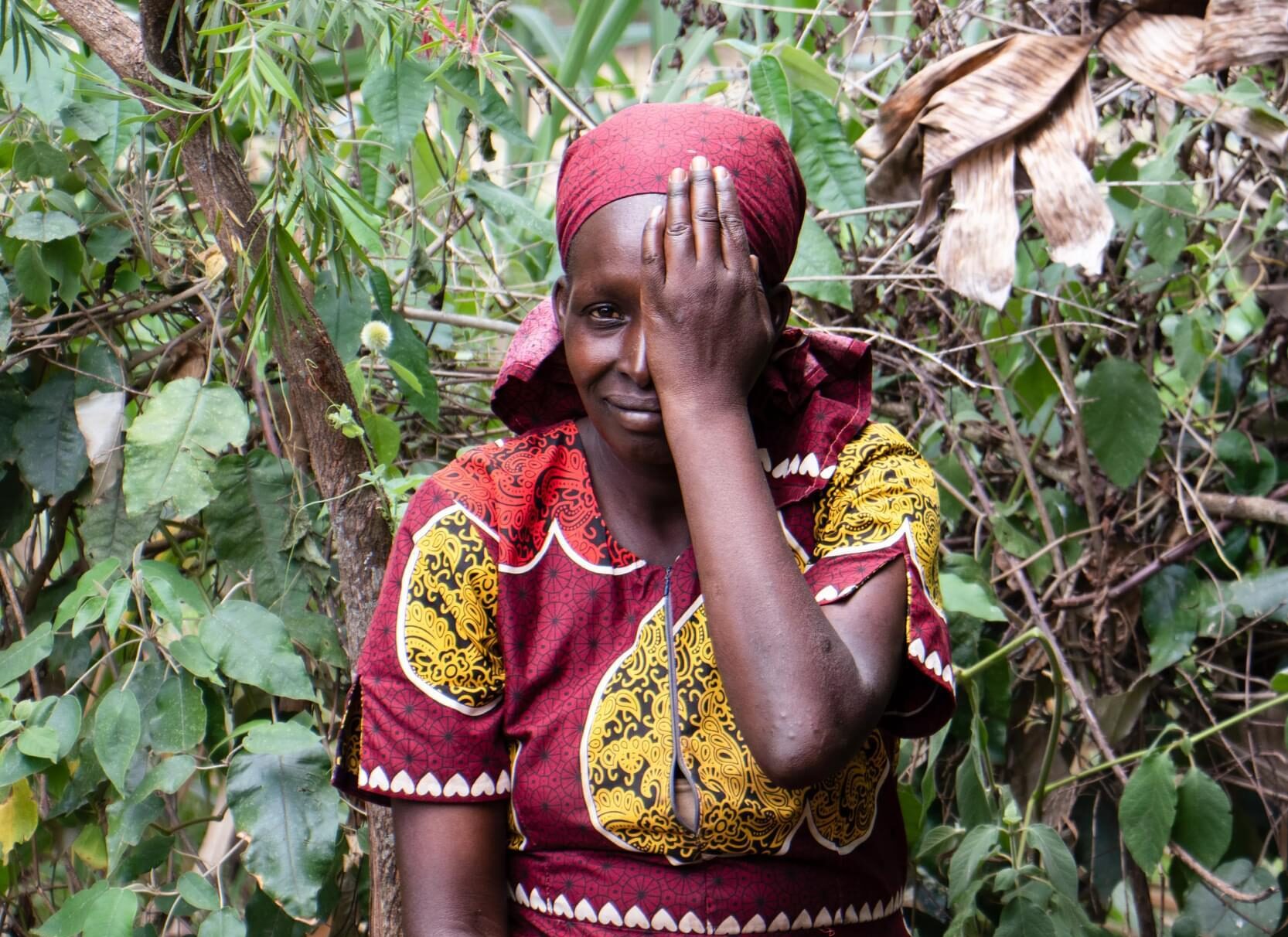 A woman having her eye screened as part of the Vision Impact Project in Bomet, with one hand over her left eye, and sitting in front of some trees.