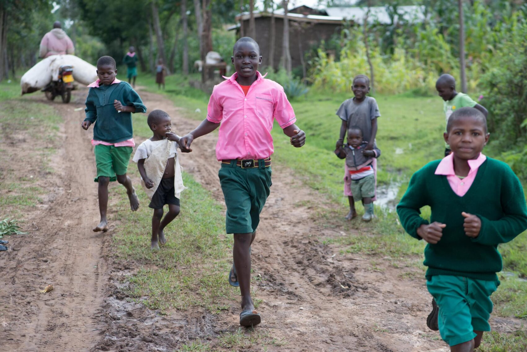 Children run towards the camera in rural Kenya. They are wearing pink and green school uniforms.