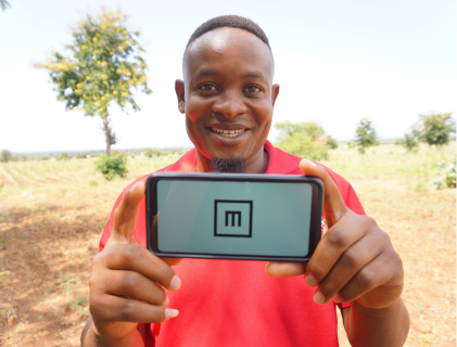 Benson Paul Magina is standing in a rural field holding the Peek Vision app on the screening test function near to a village screening centre in Tanzania.