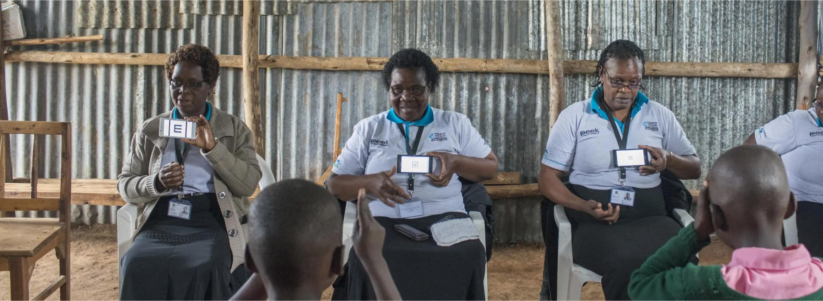 Three Kenyan women use the Peek Vision screening app to test the vision of children at a rural primary school in Kenya.