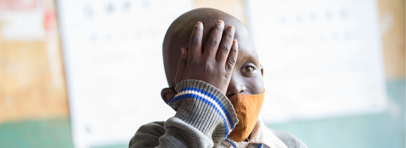 A child has his vision screened at a school in Kenya. He holds a hand to cover one eye to test the strength of his other eye.