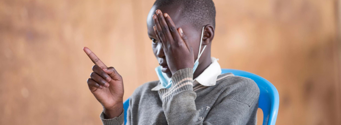 A boy covers his eye and points as part of vision screening in a Kenyan school