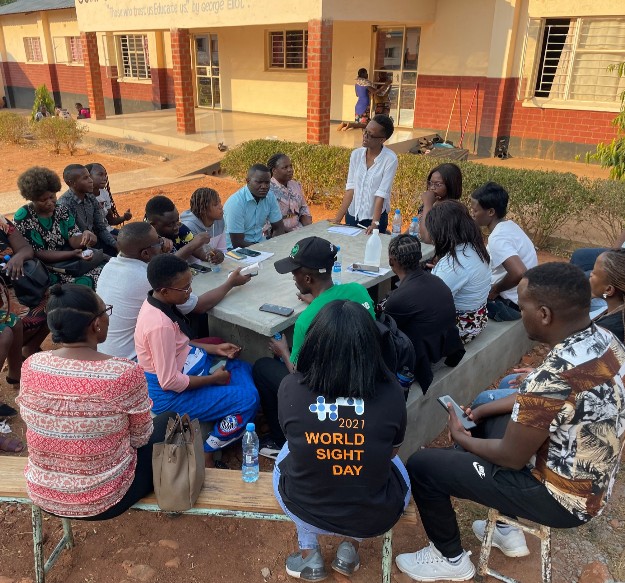 A group of seated people in discussion with one standing Peek team member