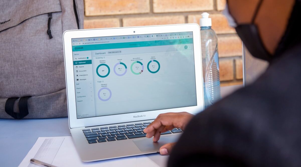 A user looking at the Peek Admin web portal on a laptop. It displays information in circles on a dashboard.